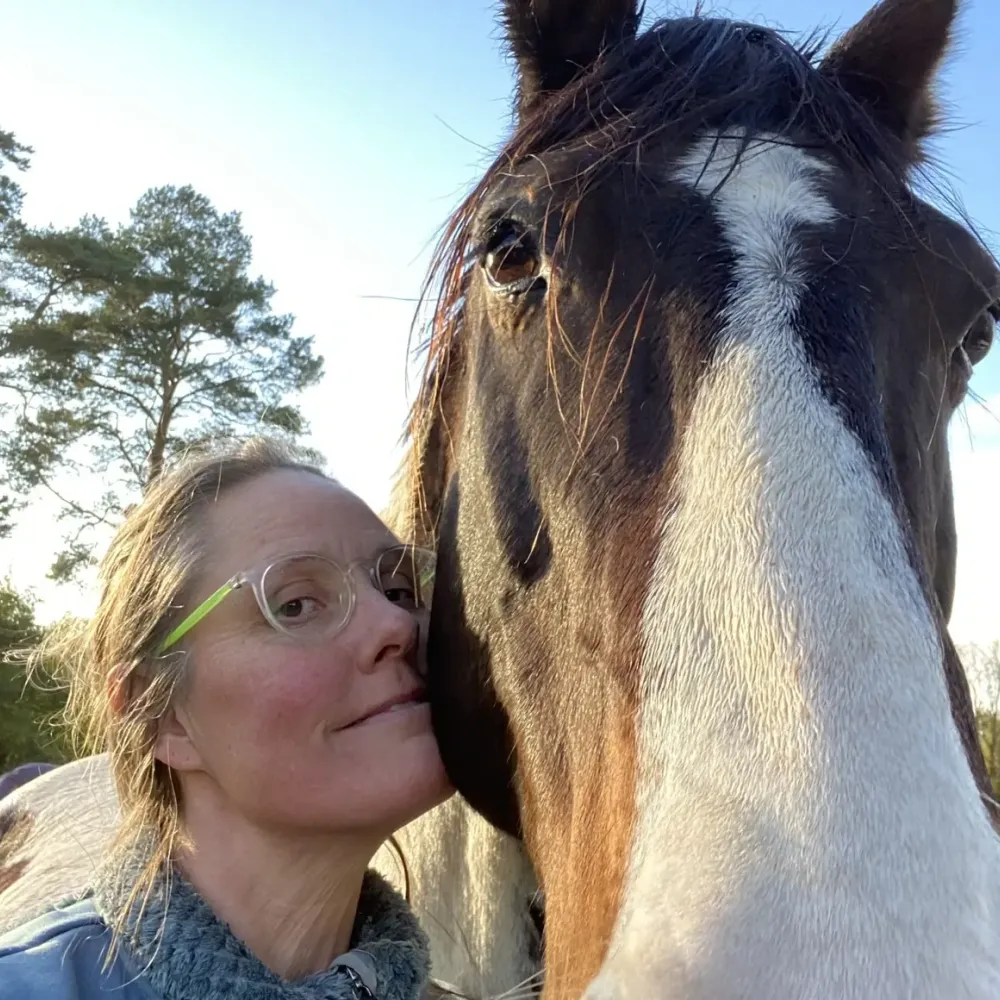 Jessica Bergman tillsammans med en häst utomhus i kvällsljus